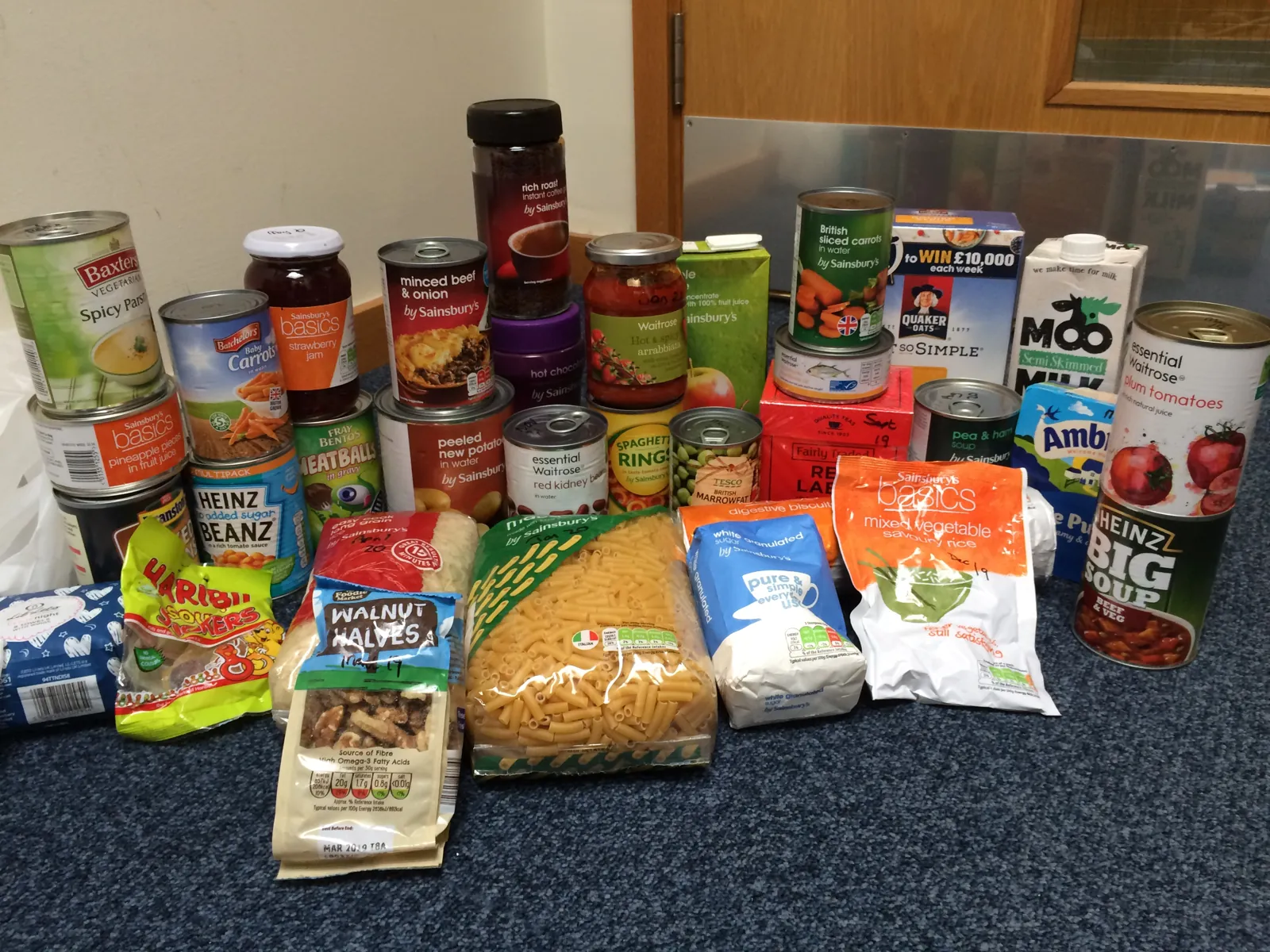 The contents of a food parcel laid out: tins of soup, meat, vegetables and fruit, pasta, rice, cereal, jam, coffee, tea, sugar, long-life milk and juice